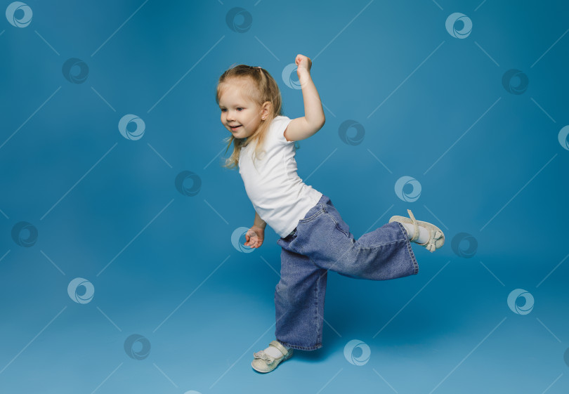 Скачать Маленький милый ребенок, девочка 2-3 лет, одетая в светлую одежду, танцует на голубом фоне, студийный портрет для детей. День матери, любовь, семья, фотосток Ozero