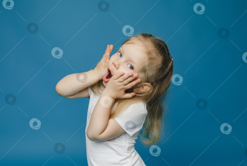 Скачать симпатичная маленькая девочка 2-3 лет со светлыми волосами смотрит в камеру, закрывает лицо руками и удивляется. фотосток Ozero