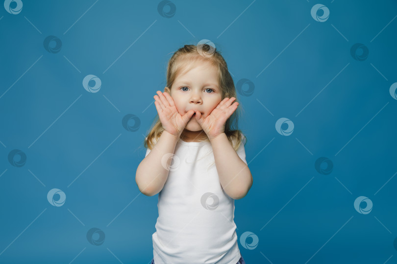Скачать симпатичная маленькая девочка 2-3 лет со светлыми волосами смотрит в камеру, закрывает лицо руками и удивляется. фотосток Ozero