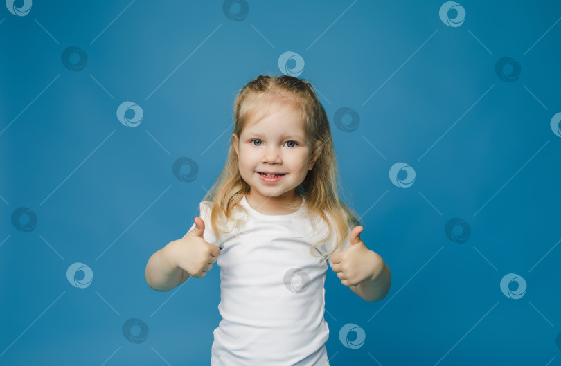 Скачать Фотография жизнерадостной счастливой девочки 2-3 лет, показывающей большой палец вверх, что означает "рекомендуется", выделенная на синем фоне. фотосток Ozero