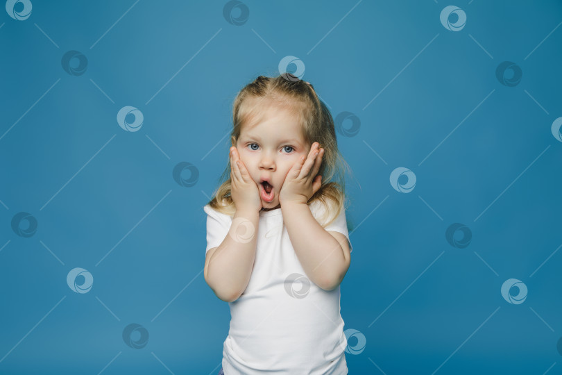 Скачать симпатичная маленькая девочка 2-3 лет со светлыми волосами смотрит в камеру, закрывает лицо руками и удивляется. фотосток Ozero