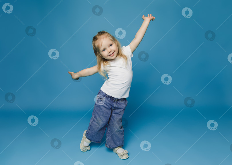Скачать Маленький милый ребенок, девочка 2-3 лет, одетая в светлую одежду, танцует на голубом фоне, студийный портрет для детей. День матери, любовь, семья, фотосток Ozero