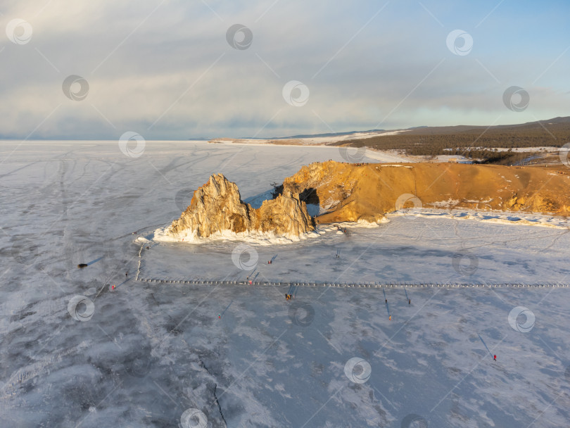 Скачать Небо затянуто облаками, солнце садится, создавая мрачную атмосферу. Вид на гору Шаманка, озеро Байкал зимой фотосток Ozero
