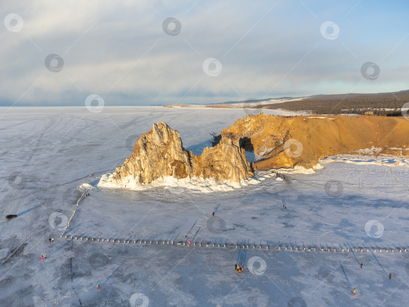 Скачать Небо затянуто облаками, солнце садится, создавая мрачную атмосферу. Вид на гору Шаманка, озеро Байкал зимой фотосток Ozero