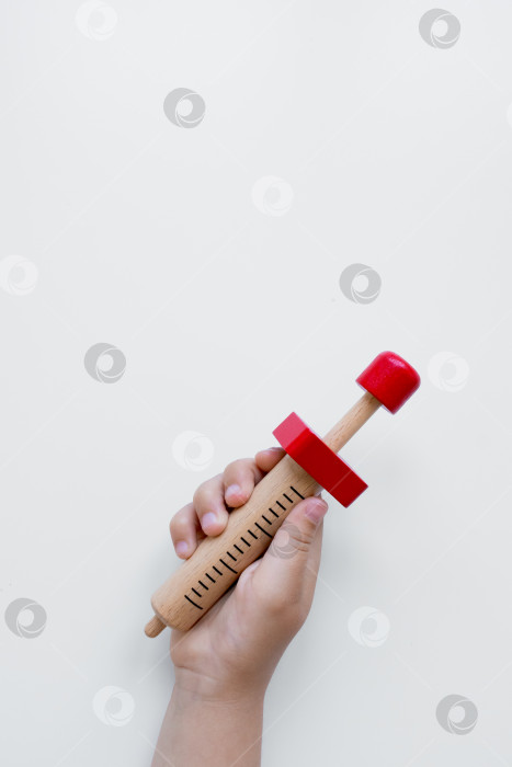Скачать Детская рука держит деревянный игрушечный шприц с красными деталями на белом фоне фотосток Ozero