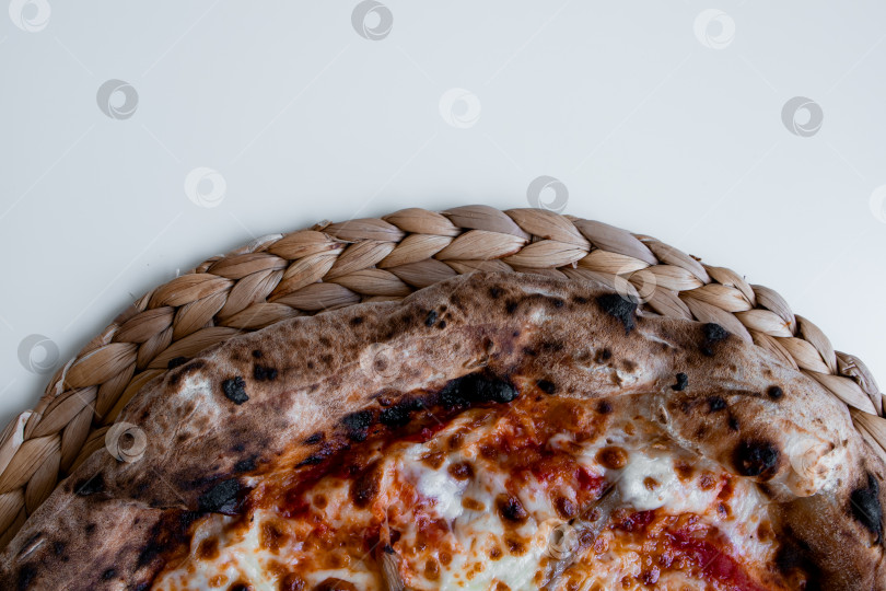 Скачать Крупный план пиццы "Маргарита" с хрустящей корочкой на плетеном коврике фотосток Ozero