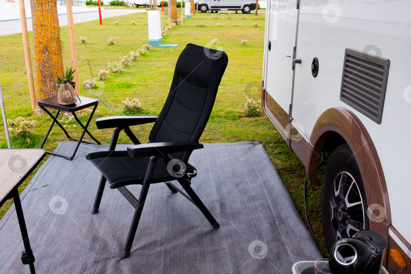 Скачать Удобное кресло для отдыха на открытом воздухе от camper в живописном месте для кемпинга с травой и деревьями фотосток Ozero