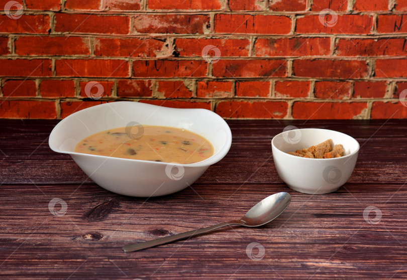 Скачать Тарелка грибного супа-пюре с сыром и пшеничными гренками на деревянном столе, ложка рядом. фотосток Ozero