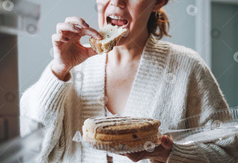 Скачать Привлекательная дружелюбная брюнетка средних лет в уютном кардигане ест торт из холодильника на кухне у себя дома фотосток Ozero