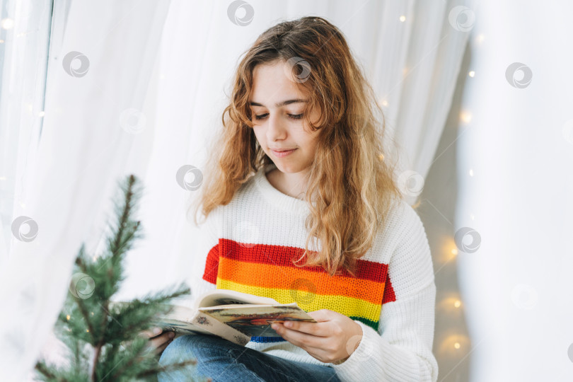 Скачать Красивая девочка-подросток читает книгу, сидя на подоконнике в уютной детской комнате фотосток Ozero