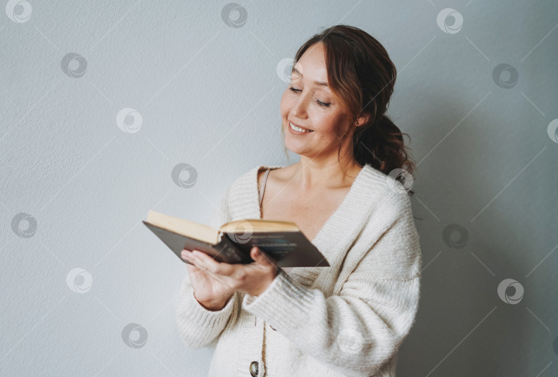 Скачать Привлекательная дружелюбная улыбающаяся брюнетка среднего возраста, читающая книгу дома, создает уютную атмосферу холодного времени года фотосток Ozero
