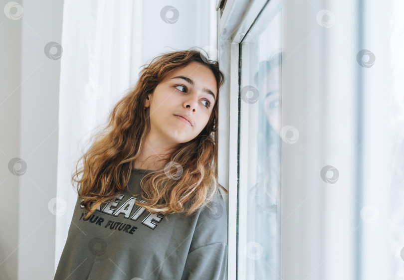 Скачать Красивая грустная несчастная девочка-подросток с вьющимися волосами сидит на подоконнике фотосток Ozero