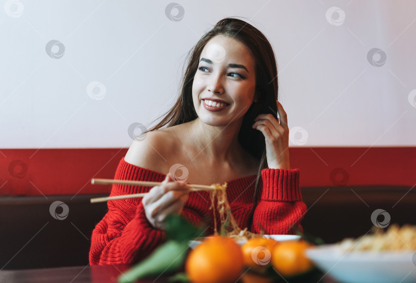 Скачать Красивая улыбающаяся молодая азиатка в красной одежде ест азиатскую кухню в китайско вьетнамском ресторане фотосток Ozero