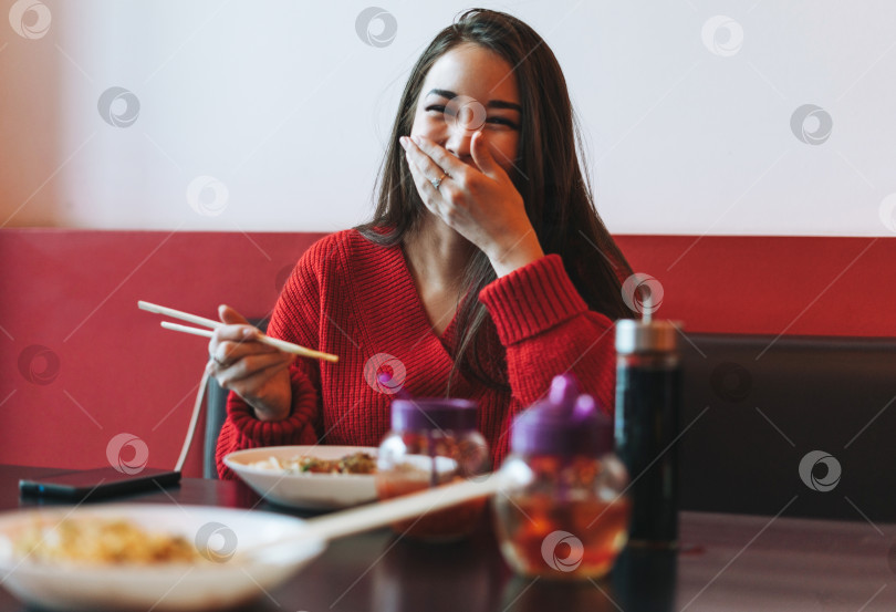 Скачать Красивая улыбающаяся молодая азиатка в красной одежде ест азиатскую еду бамбуковыми палочками для еды в китайско-вьетнамском ресторане фотосток Ozero