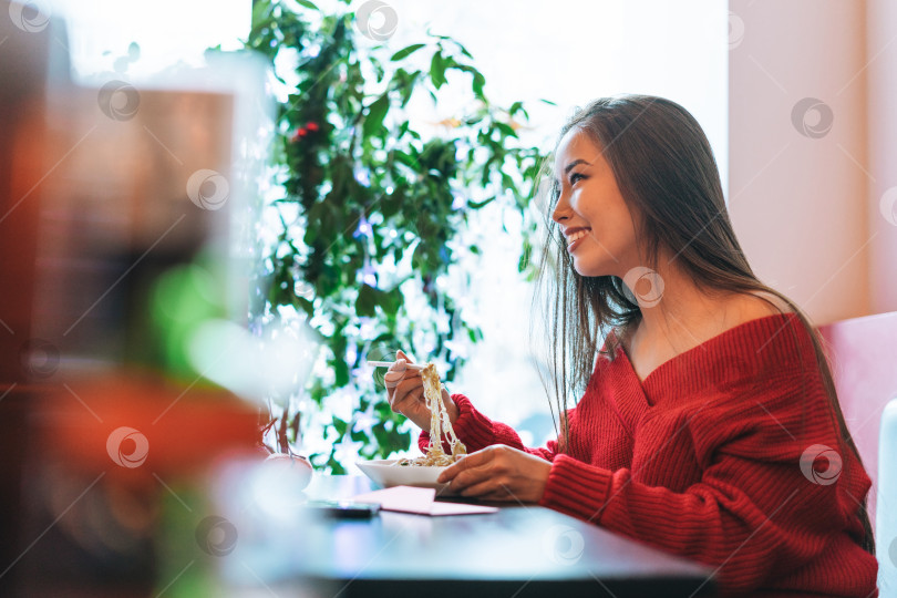 Скачать Красивая улыбающаяся молодая азиатка в красной одежде ест азиатскую кухню в китайско вьетнамском ресторане фотосток Ozero