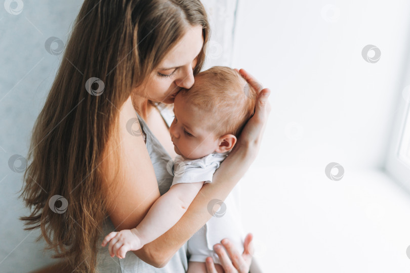 Скачать Молодая женщина-мама с длинными волосами, держащая на руках маленькую девочку у окна дома фотосток Ozero