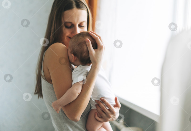 Скачать Молодая женщина-мама с длинными волосами, держащая на руках маленькую девочку у окна дома фотосток Ozero