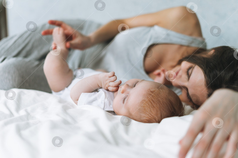 Скачать Молодая мама развлекается с милой малышкой на кровати, естественные тона, любовные эмоции фотосток Ozero
