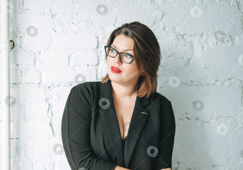 Скачать Красивая улыбающаяся молодая женщина бизнес-леди в очках и черном пиджаке на фоне белой стены фотосток Ozero