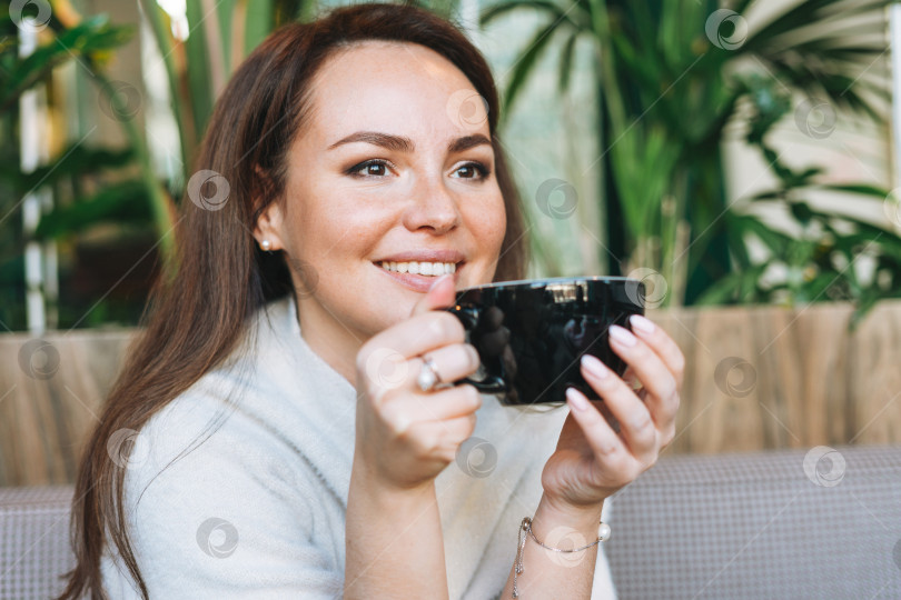 Скачать Привлекательная молодая брюнетка, улыбающаяся женщина в белом повседневном платье с чашкой кофе в руках в кафе фотосток Ozero