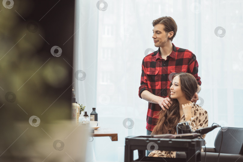 Скачать Парикмахер-стилист укладывает длинные волосы красивой молодой азиатской женщине в салоне красоты, рабочий момент фотосток Ozero
