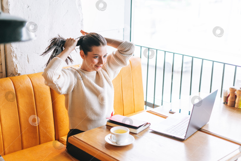 Скачать Привлекательная молодая брюнетка улыбающаяся женщина студентка-фрилансер за чашкой чая с ноутбуком работает в кафе фотосток Ozero