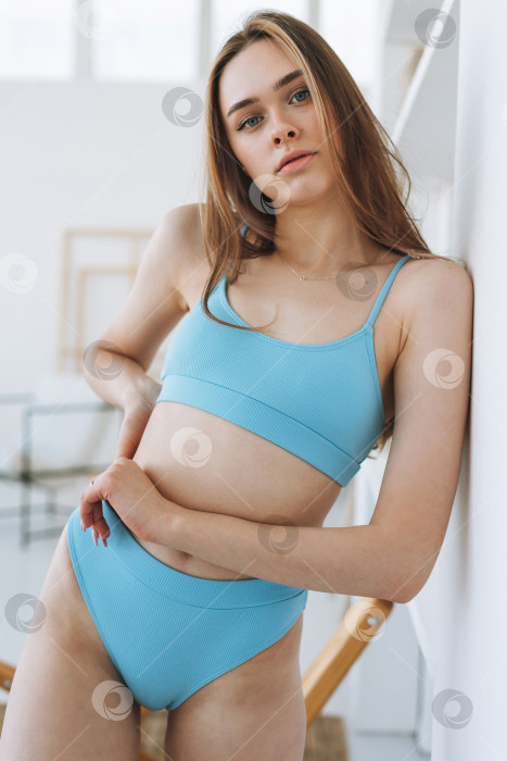 Скачать Красивая молодая женщина-фотомодель с длинными волосами в светло-голубом спортивном бесшовном нижнем белье в рубчик смотрит в камеру в яркой студии фотосток Ozero