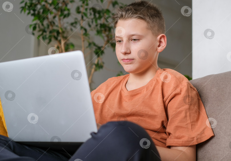Скачать Мальчик-подросток учится или играет в игру на фоне домашнего интерьера ноутбука. Парень делает домашнее задание и печатает на ноутбуке фотосток Ozero