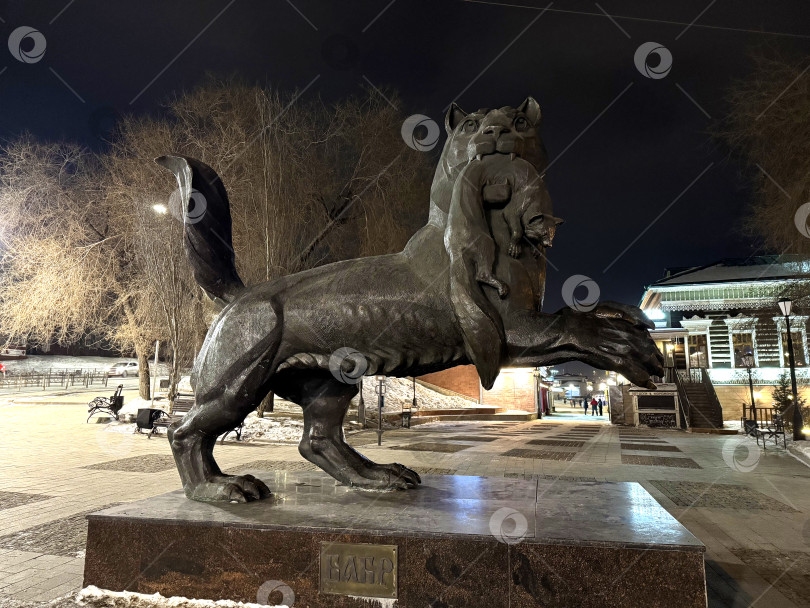 Скачать Иркутск, Россия - 15.02.2025 - Статуя Бабра в Иркутске ночью в зимнем окружении исторической архитектуры фотосток Ozero