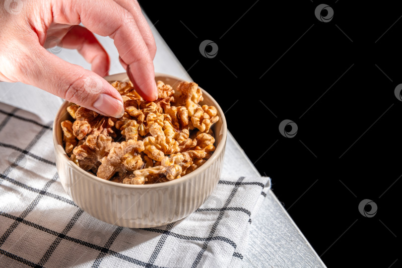 Скачать Женская рука тянется к миске с грецкими орехами, выбирая один из горки на клетчатой салфетке, готовый к употреблению в качестве полезного перекуса или ингредиента в рецепте фотосток Ozero