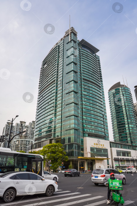 Скачать Шанхай, Китай - 1 апреля 2025 года: Отель Eton Hotel Shanghai в деловом районе Пудун с оживленным городским движением и водителем-курьером на оживленном городском перекрестке фотосток Ozero