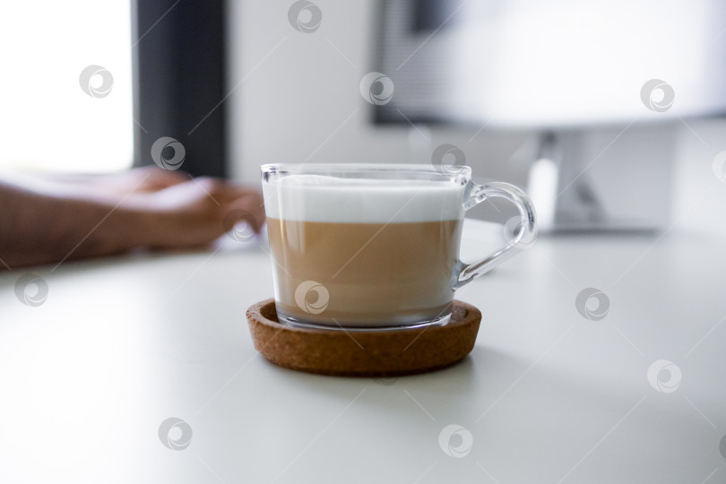 Скачать Капучино в прозрачной кружке на столе с мужской рукой и монитором компьютера на заднем плане фотосток Ozero
