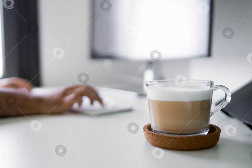 Скачать Человек, работающий за письменным столом с чашкой латте из прозрачного стекла в светлом офисе фотосток Ozero