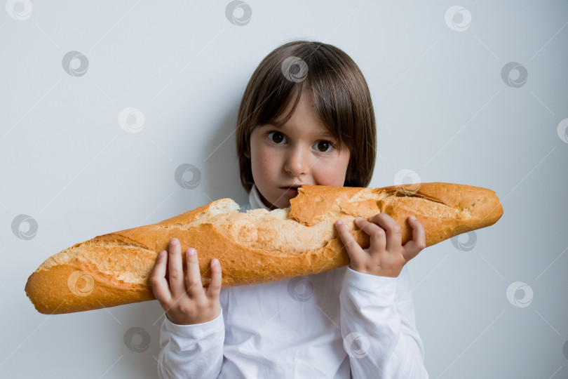 Скачать Маленький кавказский ребенок держит в руках большой багет на простом белом фоне фотосток Ozero