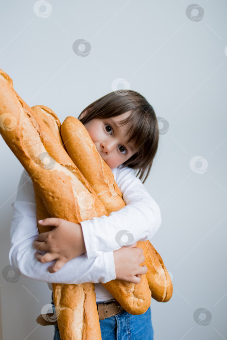 Скачать Маленький кавказский ребенок с задумчивым выражением лица обнимает большие багеты фотосток Ozero