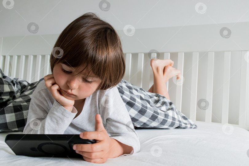 Скачать Молодой кавказский ребенок отдыхает на кровати с планшетом в удобной пижаме фотосток Ozero