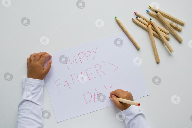 Скачать Ребенок пишет открытку с днем счастливого отца цветными карандашами на белом фоне фотосток Ozero