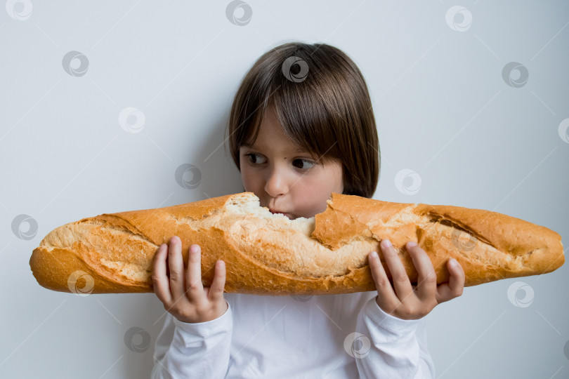 Скачать Маленький кавказский ребенок наслаждается большим багетом на белом фоне фотосток Ozero