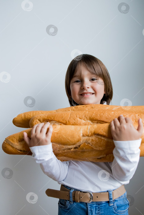 Скачать Улыбающаяся белая девушка в белой рубашке и джинсах держит в руках большие багеты фотосток Ozero