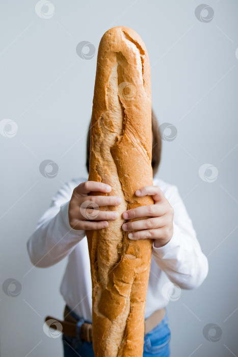 Скачать Ребенок держит перед собой большой батон багета на белом фоне фотосток Ozero