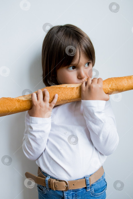 Скачать Маленький кавказский ребенок держит багет во рту на белом фоне фотосток Ozero