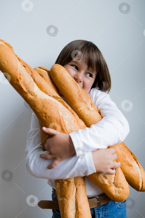 Скачать Маленький кавказский ребенок радостно держит в руках несколько багетов на белом фоне фотосток Ozero