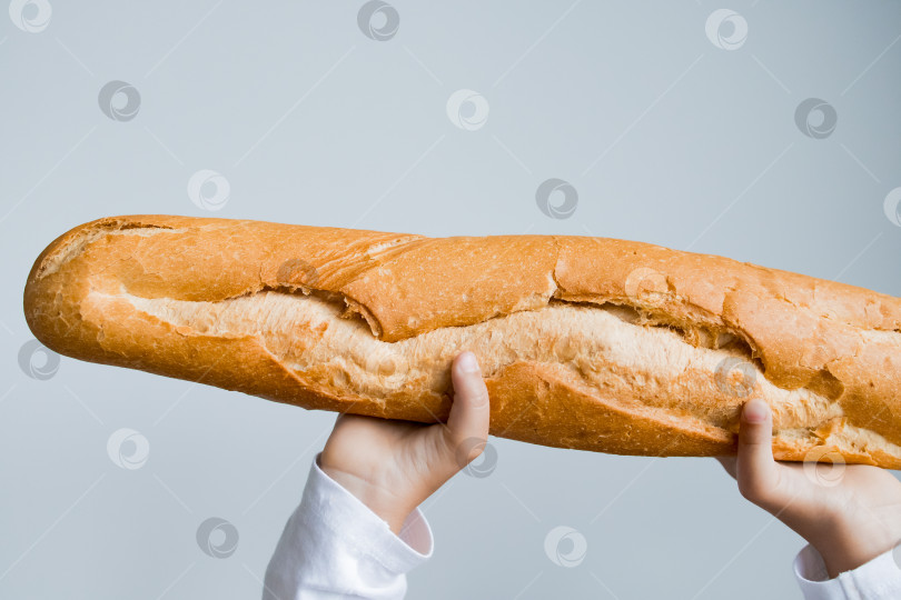 Скачать Ребенок держит большой багет на простом фоне фотосток Ozero