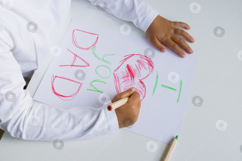 Скачать Ребенок рисует цветными карандашами сердечное послание для папы на белой бумаге. День отца фотосток Ozero