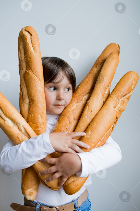 Скачать Маленький кавказский ребенок с любопытным выражением лица держит в руках несколько багетов фотосток Ozero