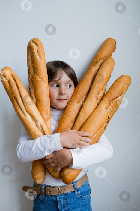 Скачать Маленький кавказский ребенок держит в руках несколько багетов на белом фоне фотосток Ozero