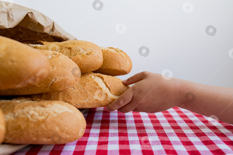 Скачать Ребенок тянется за свежеиспеченным хлебом, лежащим на клетчатой скатерти фотосток Ozero