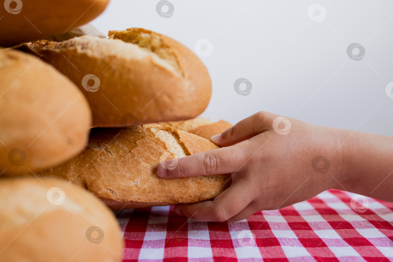 Скачать Ребенок тянется за свежеиспеченным хлебом, лежащим на клетчатой скатерти фотосток Ozero