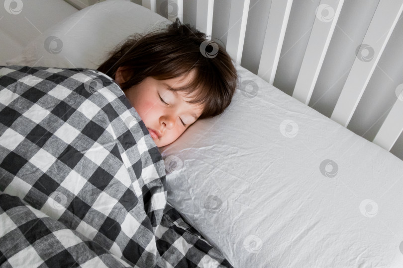 Скачать Маленький кавказский ребенок мирно спит в постели под клетчатым одеялом фотосток Ozero