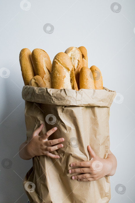 Скачать Ребенок держит в руках большой бумажный пакет, наполненный французскими багетами, на простом фоне фотосток Ozero
